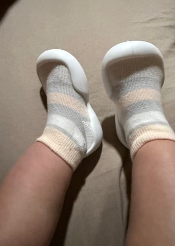 Customer's baby wearing the striped, soft Tiny Explorings™ shoe-socks, showing the flexible white soles.